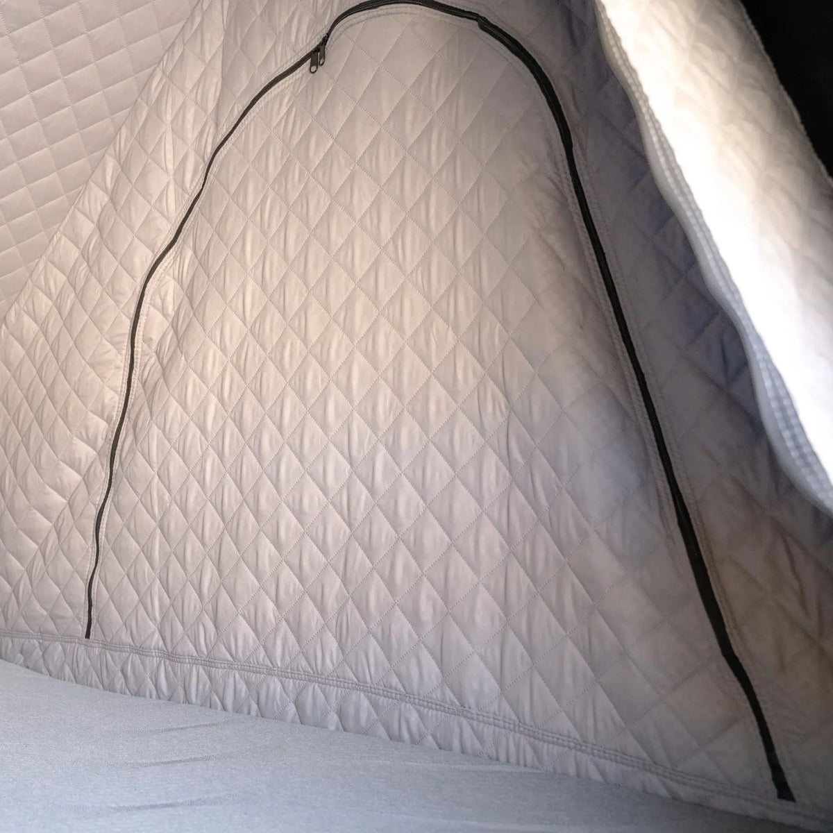 Close-up of the CVT Mt. Hood Insulation Walls—a gray, quilted fabric enclosure with an insulated liner and a large, curved zipper opening—set atop a soft, padded floor, perfect for boosting tent warmth during cold-weather camping.