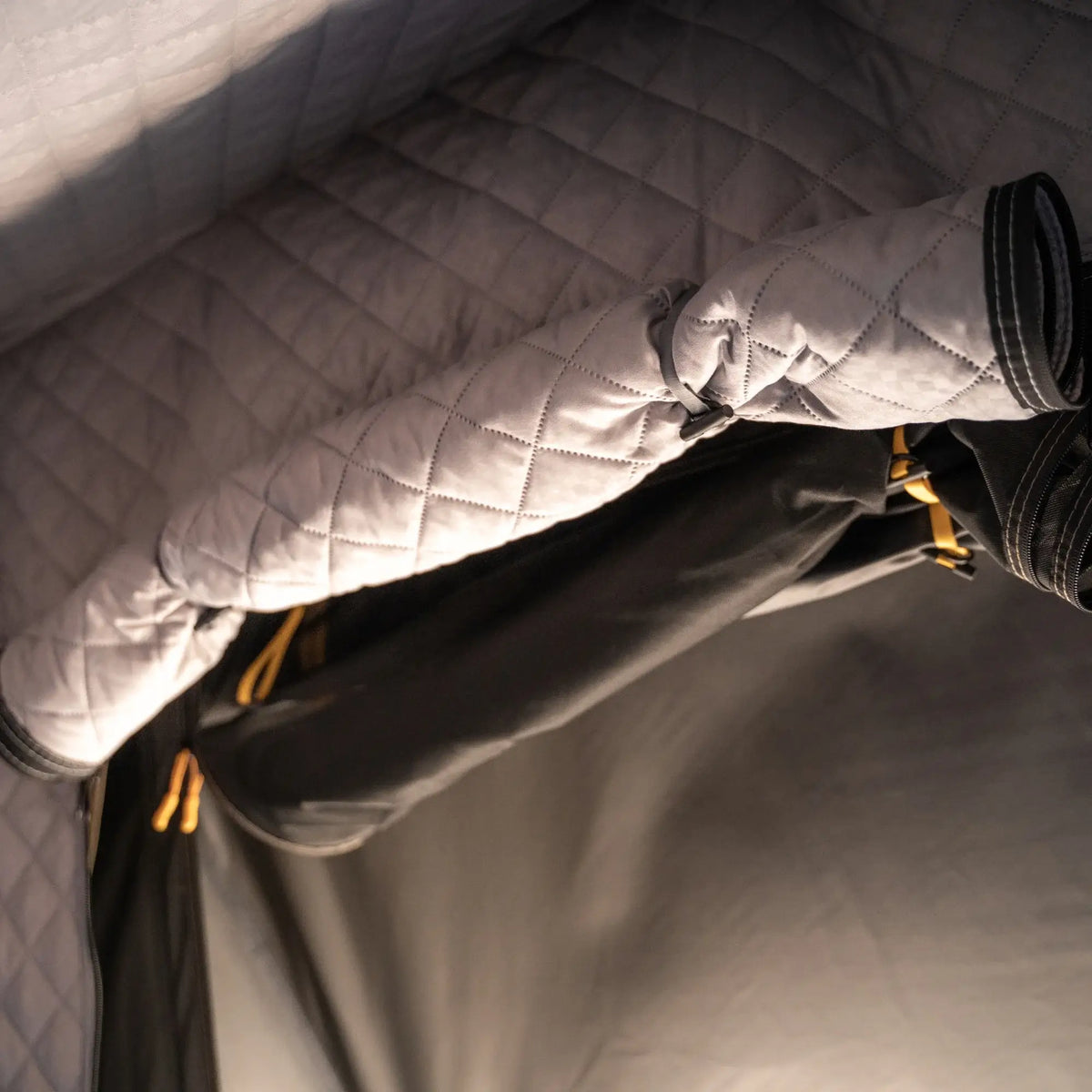 A close-up of CVT’s Mt. Hood Insulation Walls shows their quilted, padded fabric construction alongside a rolled-up insulated blanket with black and yellow accents, creating a cozy, insulated space that’s perfect for keeping your tent warm during cold-weather camping.