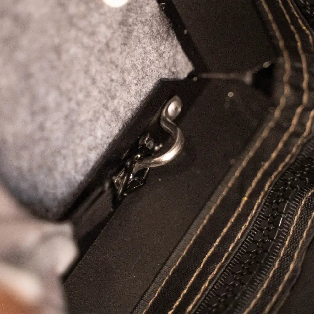Close-up of a metal hook clasp attached to the CVT Mt. Hood Insulation Walls, featuring black fabric with visible tan stitching and an insulated liner that enhances tent warmth. Some gray felt material in the background further demonstrates its suitability for cold-weather camping.