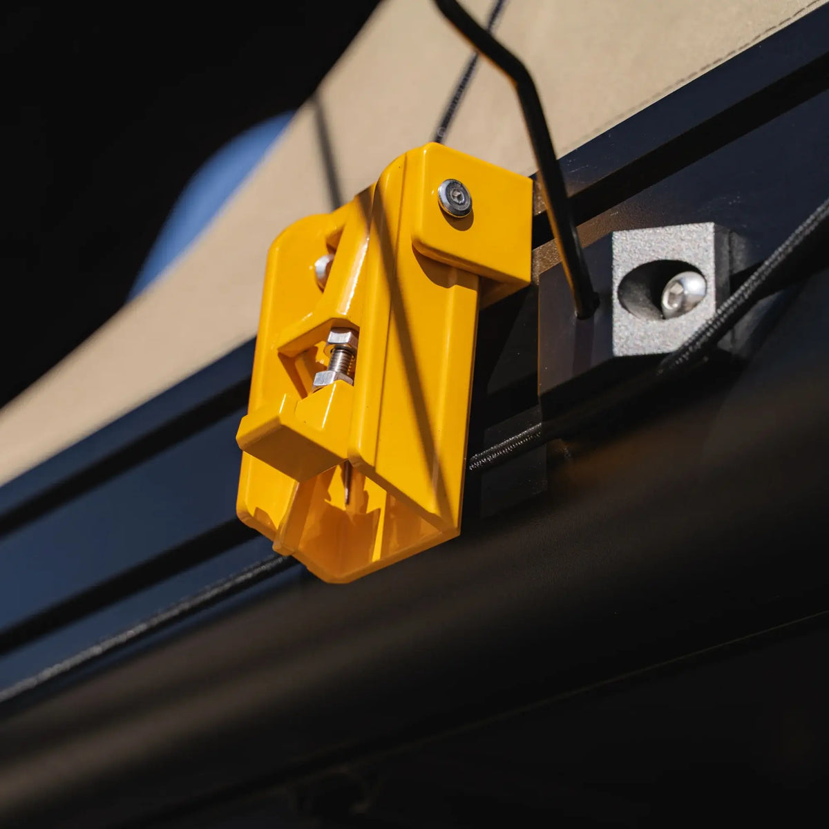 A close-up of a yellow metal latch attached to a black and beige surface, secured by a screw and bolt, with a wire running nearby—perfectly showcasing the durable hardware featured on the CVT Mt. Hood 2 Hardshell Tent, designed for rugged outdoor adventures.