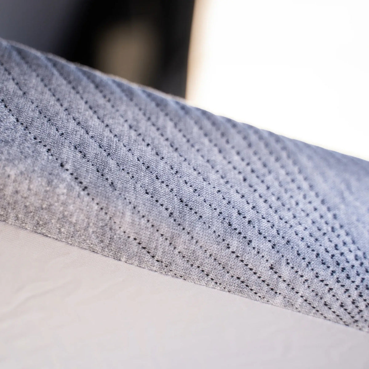 Close-up of the corner of a CVT Mt. Hood Mattress with Cover (available in 50″ and 56″), showcasing its textured gray fabric cover and white patterned side panel. The fabric includes small perforations and diagonal lines designed for breathability, ensuring a comfortable night’s sleep. Perfect as a replacement mattress for your camping adventures.