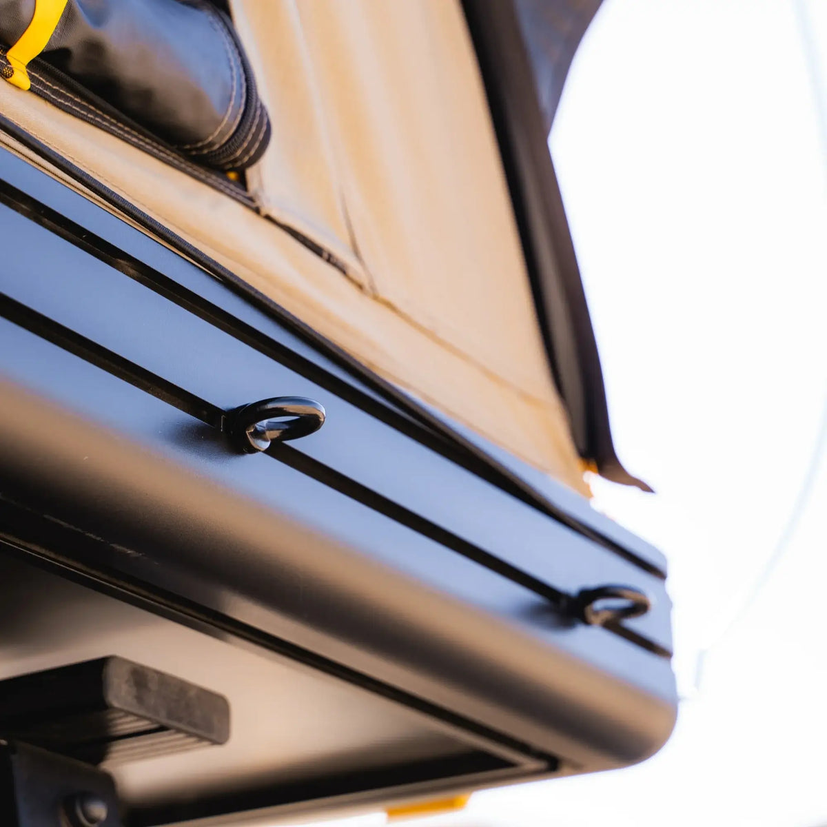 Close-up of the CVT Mt. Hood 2 Hardshell Tent’s black metal frame featuring two small loops, with part of its tan fabric rooftop visible above, photographed outdoors in bright sunlight.