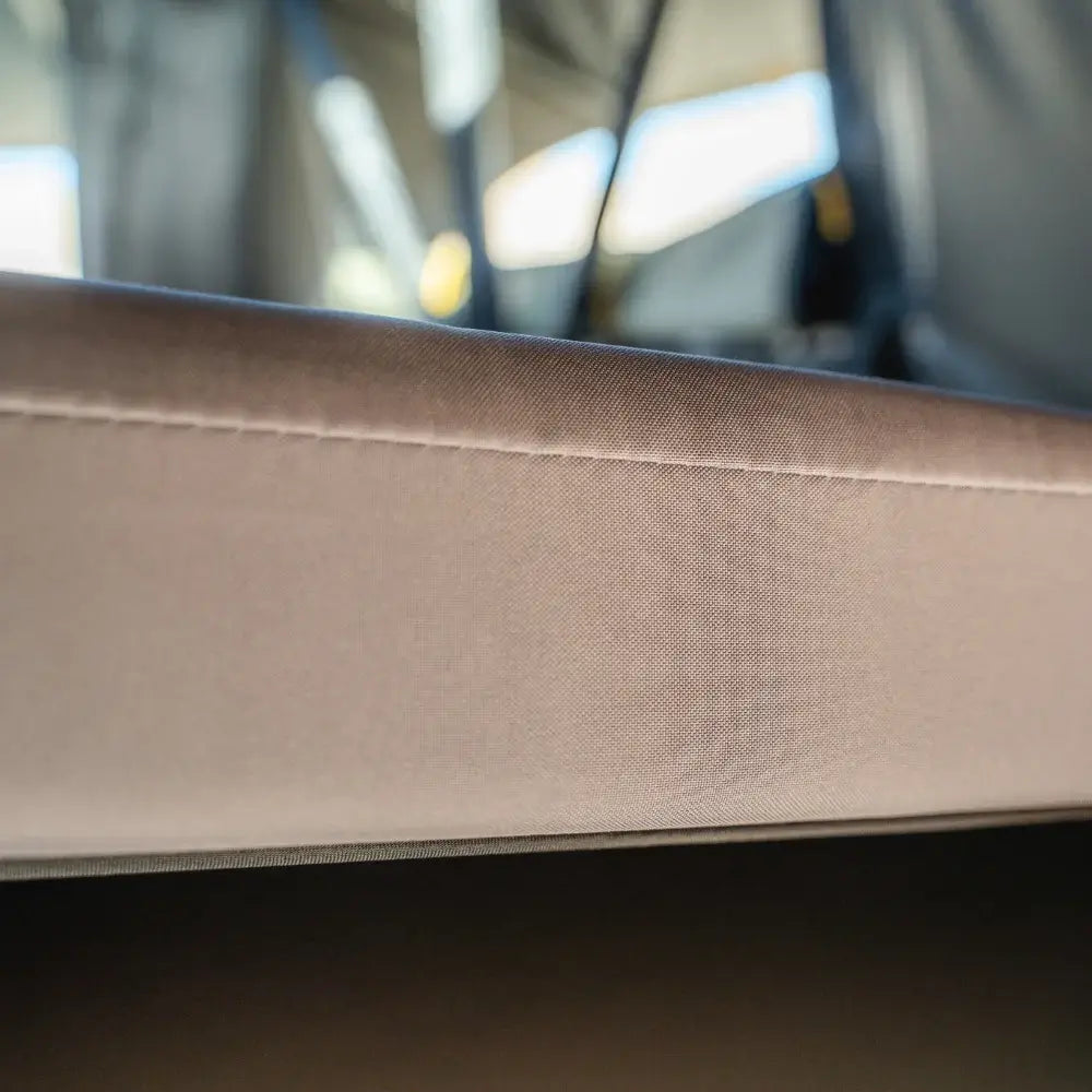 Close-up of a beige fabric edge with visible stitching on the CVT Pioneer Mattress Cover, highlighting its quality construction against a blurred background.