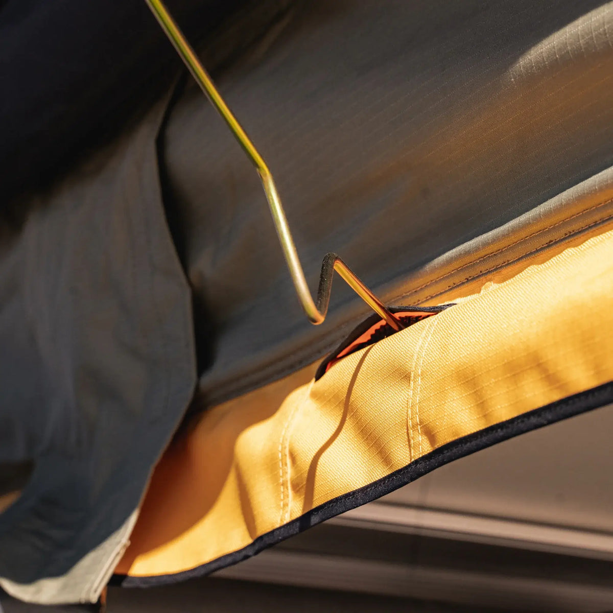 Close-up of the CVT Pioneer 2 Softshell Tent in yellow and gray being assembled, with a metal pole sliding into its reinforced corner sleeve, sunlight casting shadows across the fabric—the ideal setup for your next overland adventure.