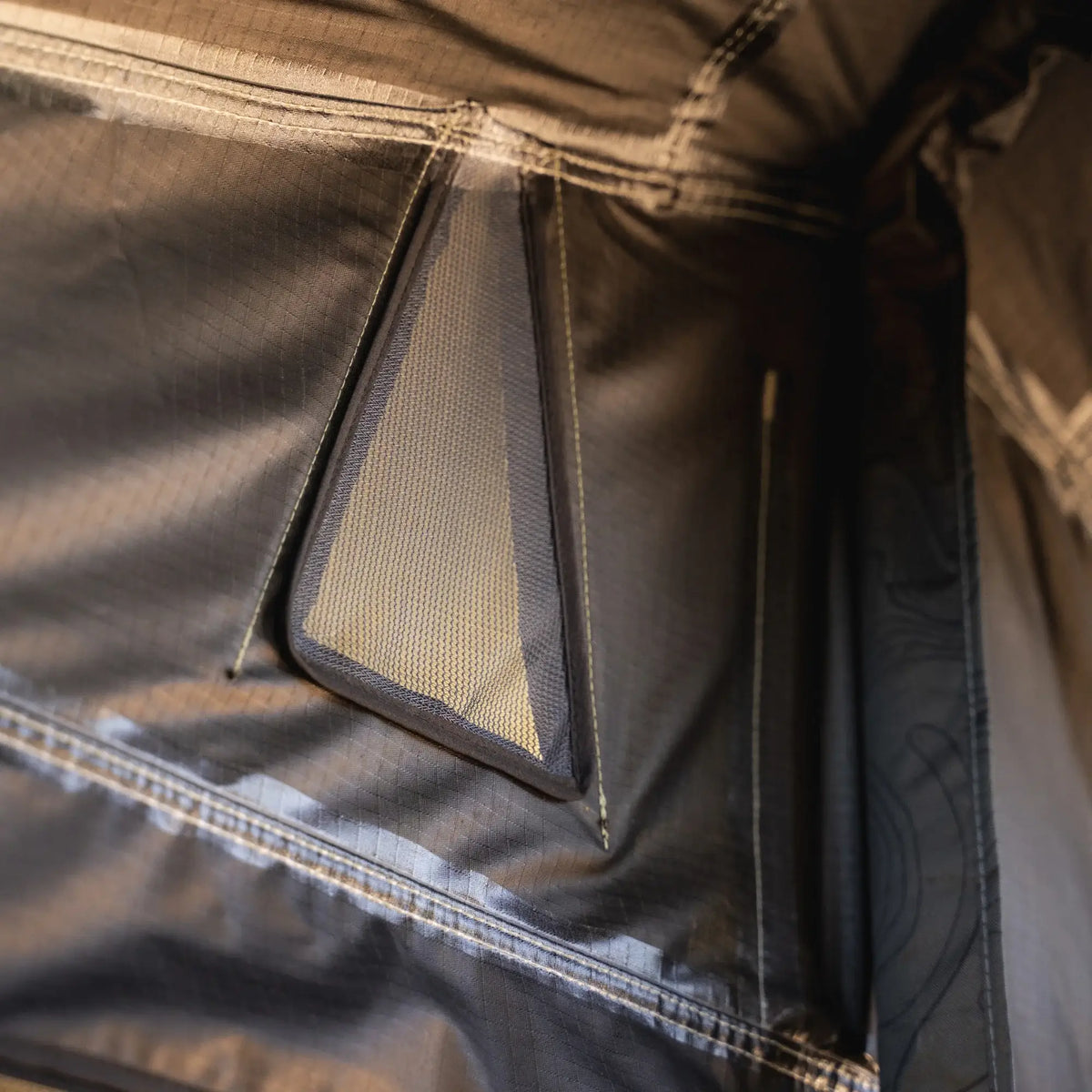 Close-up of a geometric mesh ventilation opening on the dark technical fabric of the CVT Pioneer 2 Softshell Tent, showcasing visible stitching and textured material—engineered for overland adventures.