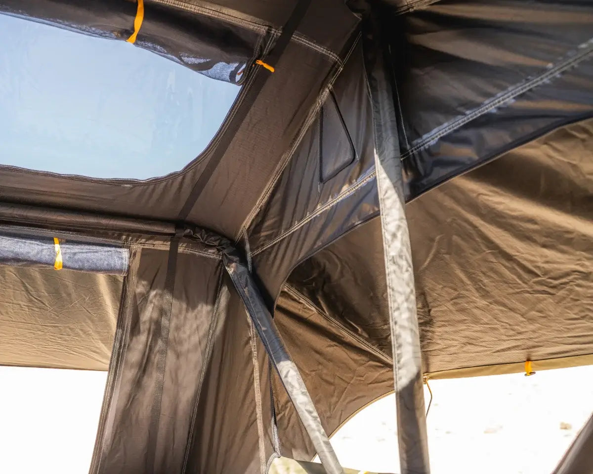 View of the inside corner of a tent, showing seams, mesh windows, yellow tie loops, and sunlight coming through a skylight.