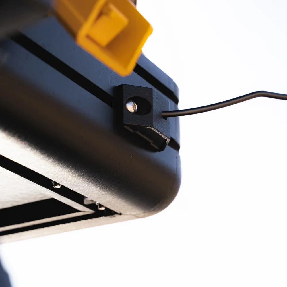 Close-up of a black plastic handle with a yellow latch and an attached cable, mounted on a surface against a bright, blurred background—an essential accessory from CVT, designed for use with Mt. Hood Spring Rod Holder - 2 Pack tents or for securing your spring rod holders.