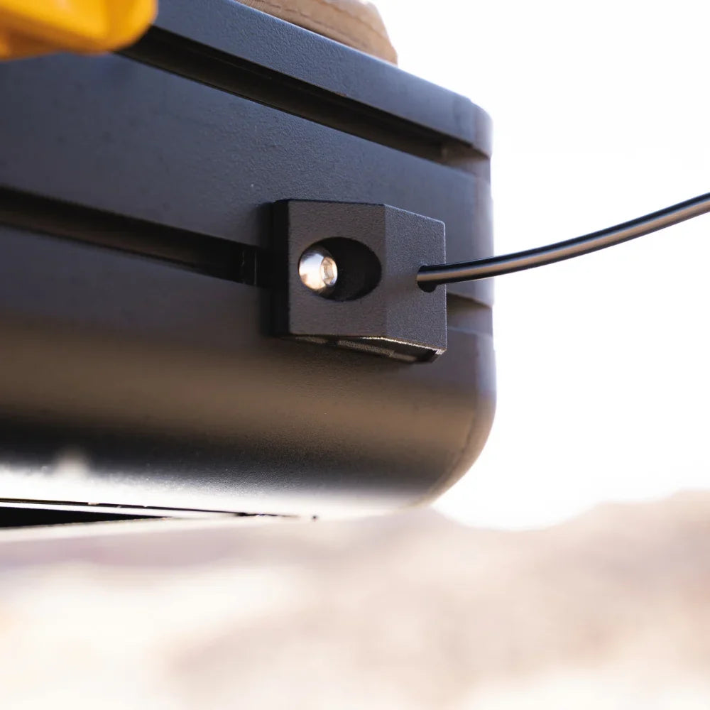A close-up of a black cable secured by a small black bracket attached to a metal surface, with a blurred outdoor background—ideal for use with tent accessories or spring rod holders such as the CVT Mt. Hood Spring Rod Holder - 2 Pack.