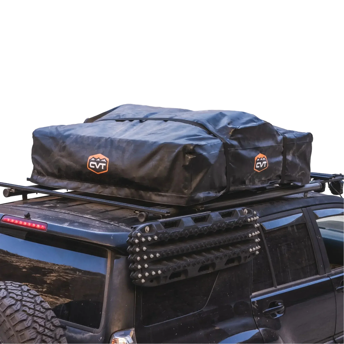 A black SUV with a black rooftop cargo bag secured on a roof rack, featuring the CVT Pioneer Travel Cover Strap Set from the Pioneer tent accessories collection for added security. Traction boards are mounted on the vehicle’s side. The background is plain white.