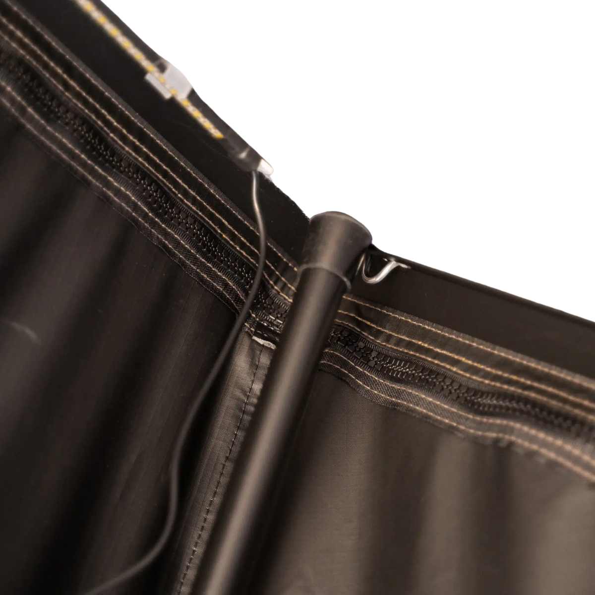 Close-up of a black metal CVT Mt. Hood/La Sal Stabilizer Interior Pole attached to black fabric with visible stitches and a hook, alongside an electrical wire, set against a plain light background—engineered for enhanced stability in CVT’s hardshell rooftop tents.