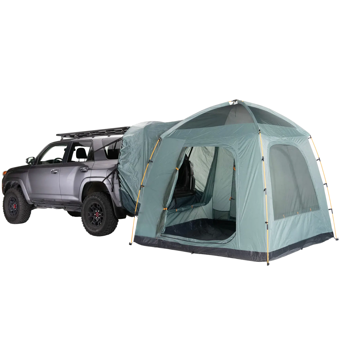 A gray SUV is parked with a large Timber Creek SUV Tent by CVT, in green, attached to its rear, creating a sheltered space that connects the vehicle to the tent. With mesh windows and a dome-style design, this tent is set up for camping—making it an ideal choice for overlanders seeking comfort and convenience on their adventures.