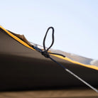 Close-up of a black cord tied in a loop, securing the edge of the CVT 180 Degree Awning—a yellow and gray outdoor shelter—against a clear blue sky, perfect for creating instant shade.