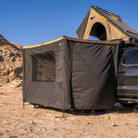 A CVT 270 Degree Awning Wall is attached to a black rooftop tent, set up on a vehicle in a desert landscape with rocky hills and a clear blue sky, providing excellent weather protection and creating the perfect outdoor camping setup for your adventure.
