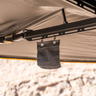 A small black fabric pouch hangs from hooks on a metal bar beneath a CVT 270 Degree Awning canopy in beige, with a blurred outdoor background.