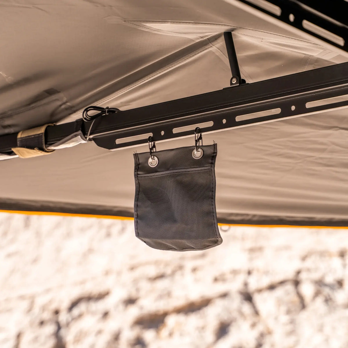 A small black fabric pouch hangs from hooks on a metal bar beneath a CVT 270 Degree Awning canopy in beige, with a blurred outdoor background.