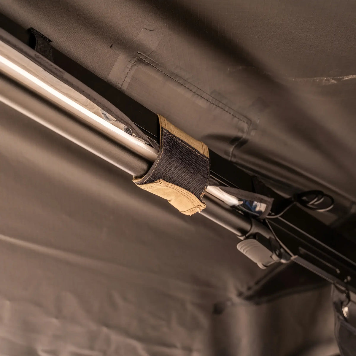 Close-up of a fabric strap securing a metal pole to a dark, textured surface, likely part of the CVT 270 Degree Awning.