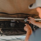 Hands adjust or retrieve a small item from the zippered mesh pocket inside a CVT Wasatch Hardshell Tent, with a cup and other overland adventure gear visible in the pocket.