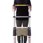 A person in a black shirt and green pants holds a compact, silver CVT Pioneer Ladder vertically against a white background.