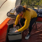 Inside a tent nestled in nature, a person in a yellow jacket and cap skillfully packs their bag using CVT Camping Cubes™, next to a cot with a sleeping bag—demonstrating how CVT’s Camping Cubes™ provide thoughtful gear organization for any outdoor adventure.