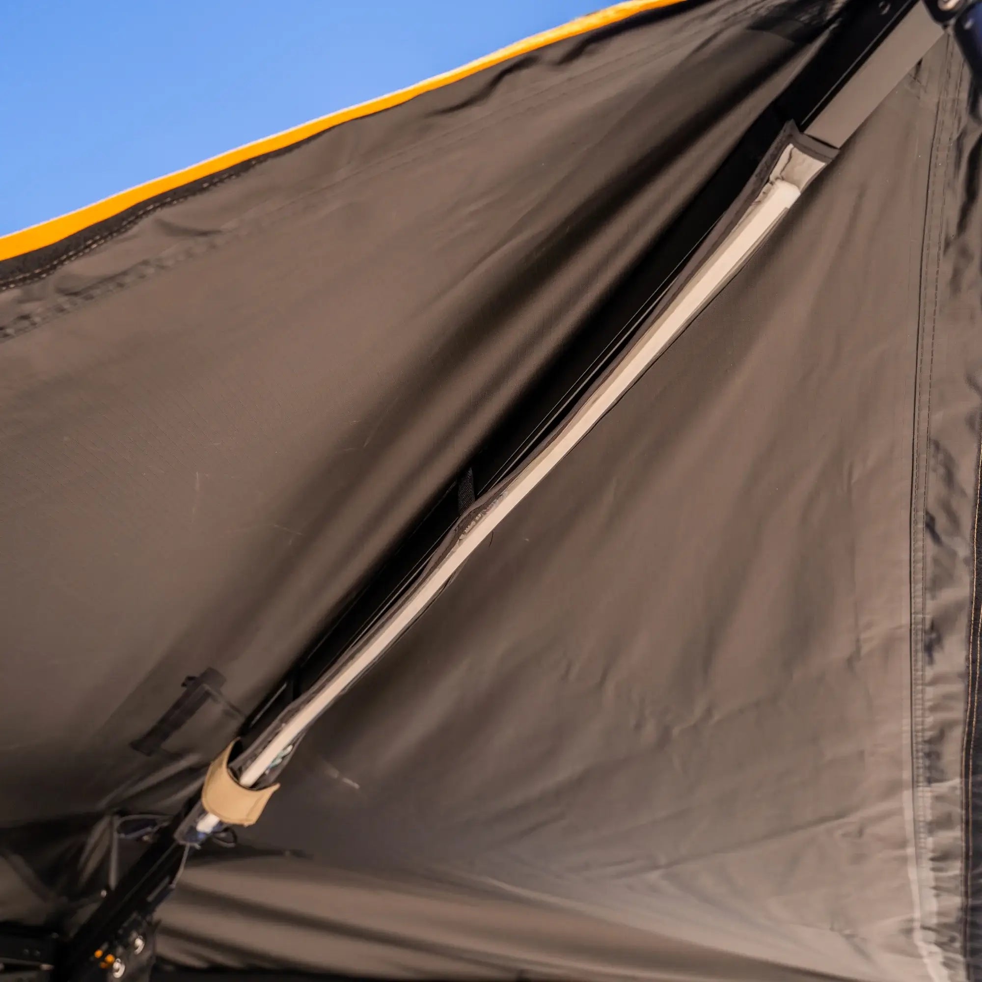 Close-up view of the interior roof of a tent, showing support poles and fabric seams under daylight, with a small portion of blue sky visible at the top edge.