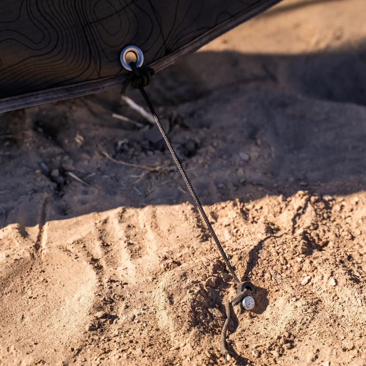 A close-up shows a corner of the CVT 270 Degree Awning Wall anchored to dry, sandy ground with a black cord and stake, highlighting its reliable weather protection.