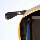 Close-up of a yellow-edged fabric on the CVT 180 Degree Awning, showing its black metal frame and a black strap with a metal grommet, set against a light background.