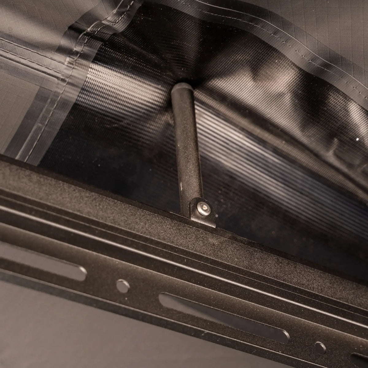 Close-up of a metal support rod attached to a black frame, holding up a section of gray and clear fabric from the CVT 270 Degree Awning.