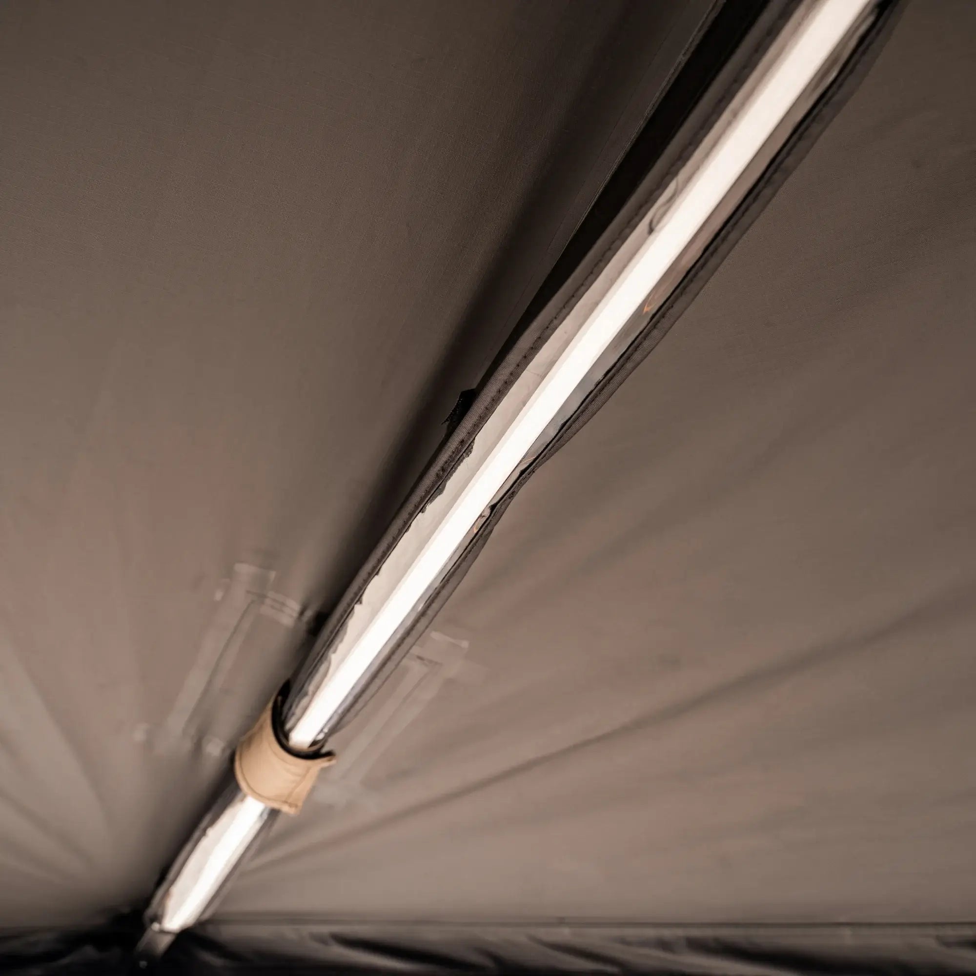 A close-up view of a fluorescent light fixture attached to a beige ceiling, with visible tape and a cable tie securing part of the fixture.