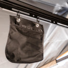 A black fabric pouch with metal grommets hangs from a metal rail using two carabiner clips inside an outdoor shelter, offering convenient storage space beneath your CVT 180 Degree Awning.
