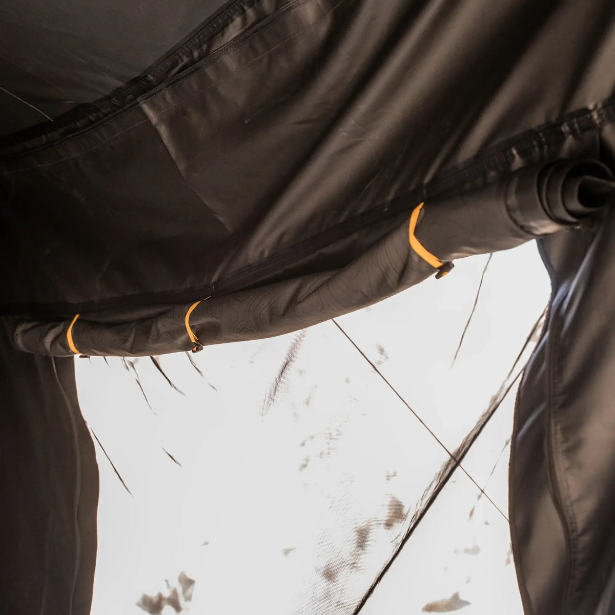 Close-up of a tent’s black fabric window rolled up and secured with yellow straps, allowing bright sunlight to stream in—perfect for pairing with the CVT 270 Degree Awning Wall to boost your weather protection.