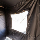 A close-up of the CVT 270 Degree Awning Wall in black fabric, featuring a large clear window rolled up and secured with elastic bands, allowing bright sunlight to enter while offering excellent weather protection.