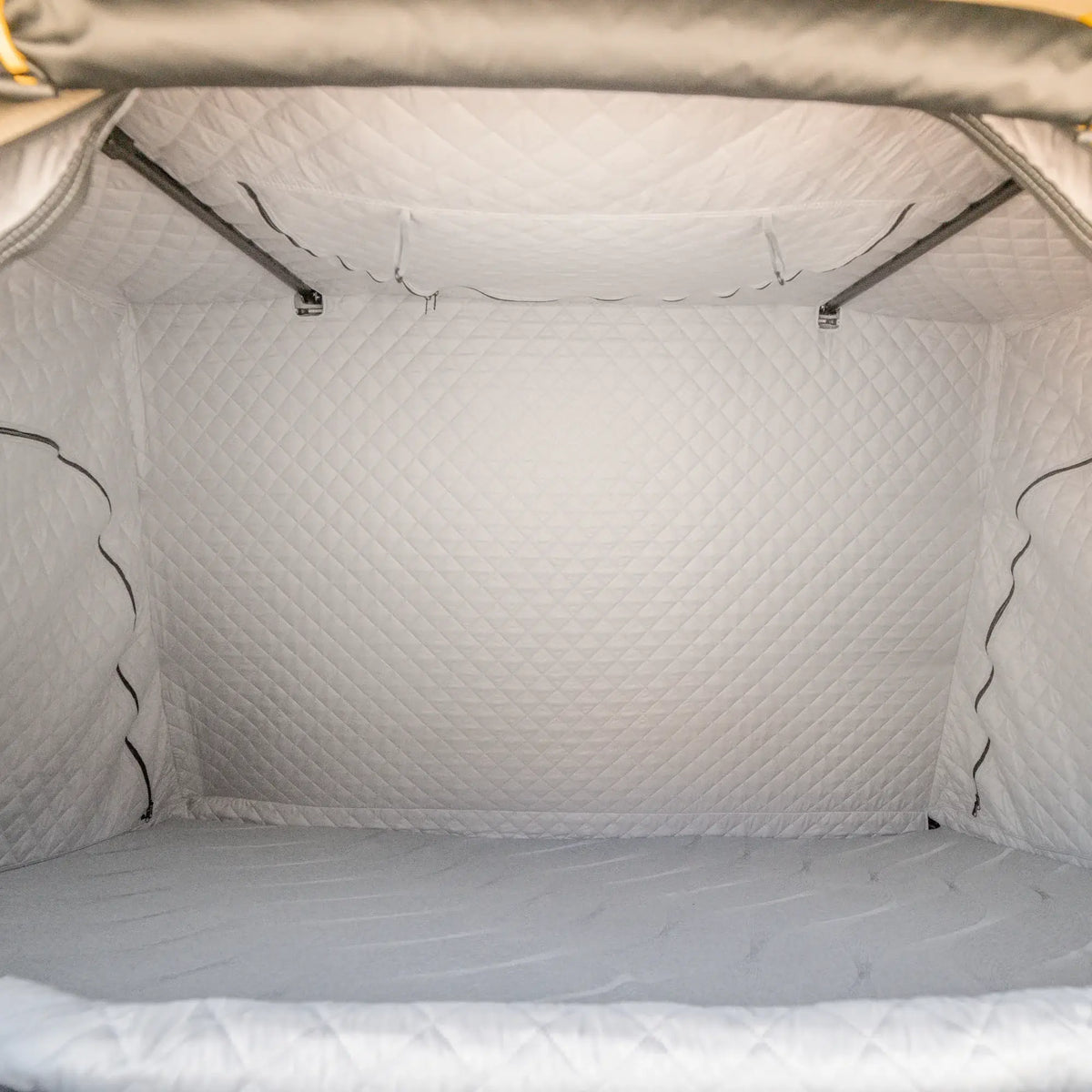 Interior view of a pop-up rooftop tent, featuring CVT’s La Sal Insulation Walls with quilted white walls and ceiling designed to enhance tent warmth. The flat cushioned sleeping area and two metal support bars across the top make it ideal for winter camping comfort.
