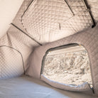 Inside a CVT tent outfitted with La Sal Insulation Walls, the quilted, insulated liner is designed to maximize warmth. An open window frames a view of the rocky, sandy landscape outside as sunlight brightens the cozy, padded interior—perfect for winter camping.