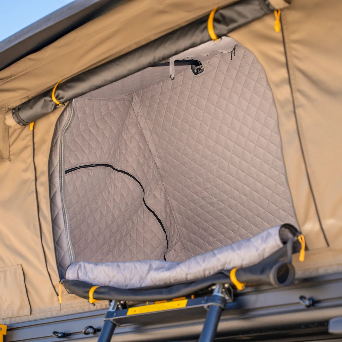 The CVT La Sal Insulation Walls feature a quilted, insulated interior lining that delivers outstanding warmth—ideal for winter camping adventures. Installed in the tent, the insulation reveals padded walls and a ladder leading up to the entrance, with eye-catching yellow accents visible on the exterior.
