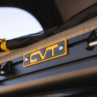 Close-up of a yellow and black CVT logo attached to a metal frame, with part of the La Sal Hardshell Tent’s fabric and yellow cord in the background—showcasing the spacious comfort and side-open design that make this innovative CVT rooftop tent stand out.
