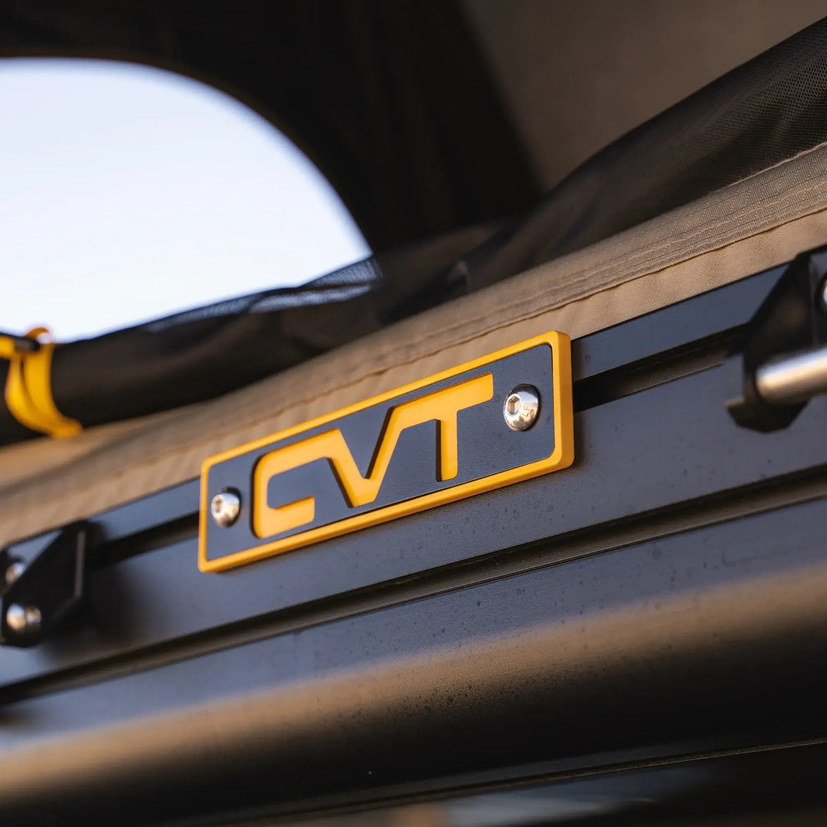 Close-up of a yellow and black CVT logo attached to a metal frame, with part of the La Sal Hardshell Tent’s fabric and yellow cord in the background—showcasing the spacious comfort and side-open design that make this innovative CVT rooftop tent stand out.