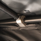 Close-up of a beige plastic bracket securing two black metal poles together, attached to a dark fabric surface with visible stitching and black tape—an essential detail in the construction of the CVT La Sal Hardshell Tent, designed for spacious comfort.