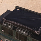 A CVT La Sal Hardshell Tent, featuring a spacious comfort side-open design and the CVT logo, is mounted on top of a green SUV parked on sandy terrain.