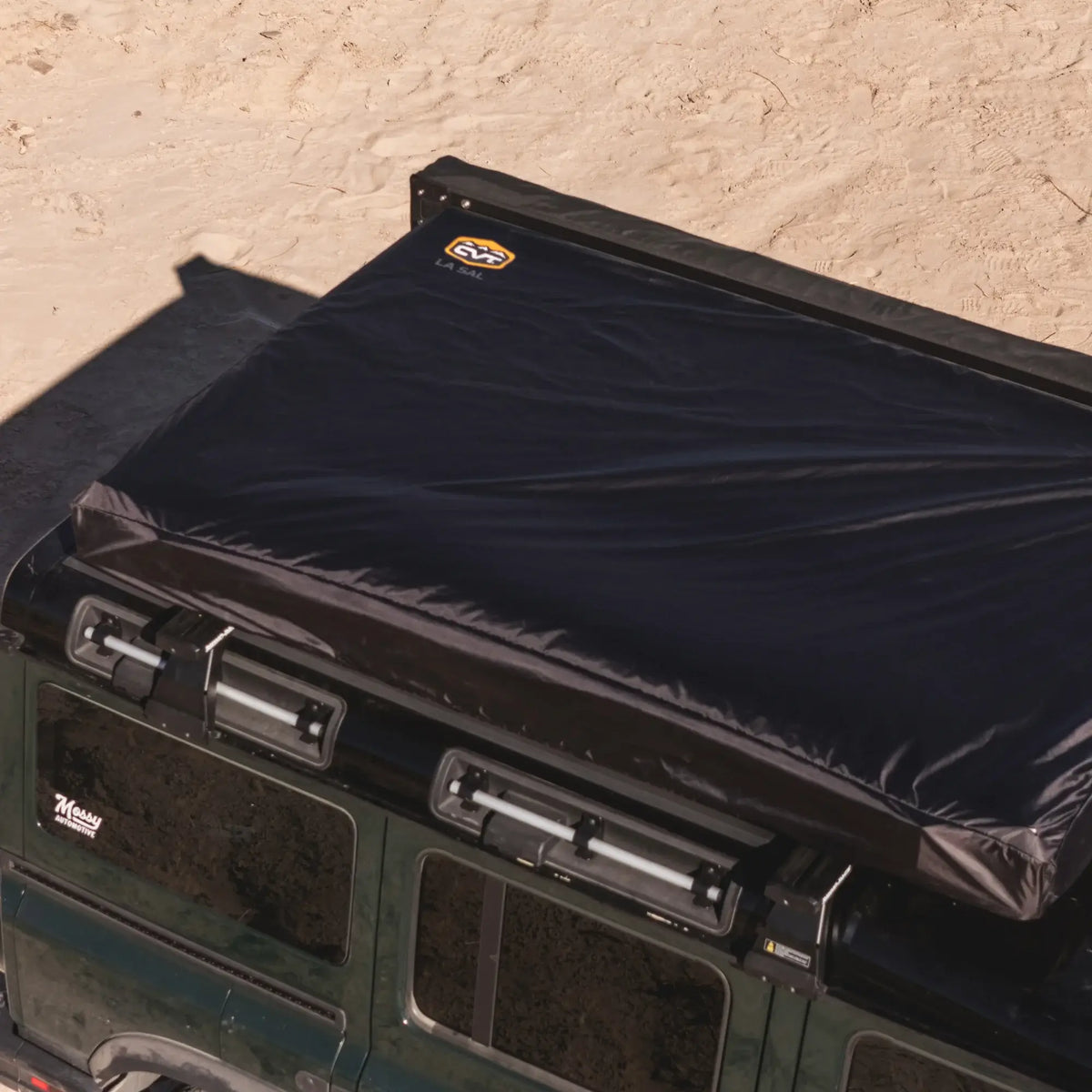 A CVT La Sal Hardshell Tent, featuring a spacious comfort side-open design and the CVT logo, is mounted on top of a green SUV parked on sandy terrain.