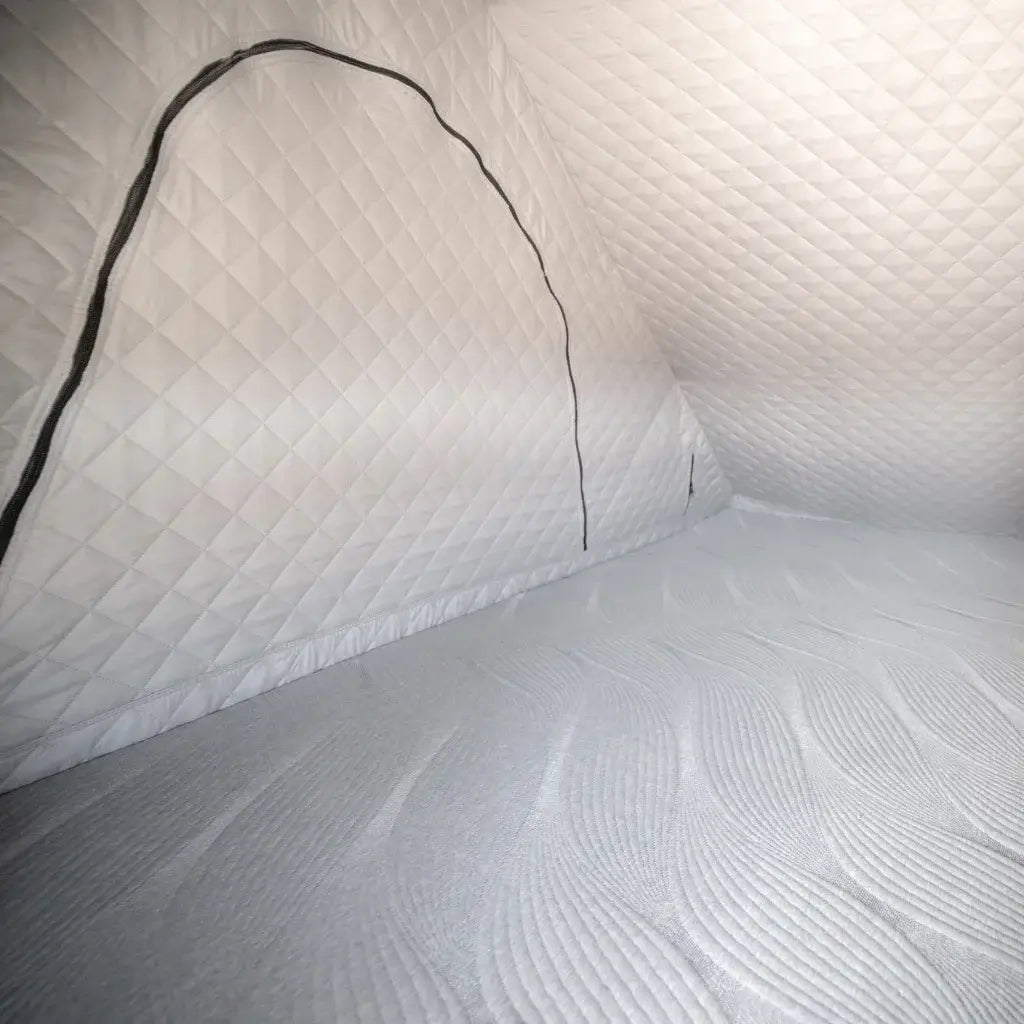 Interior of a small, insulated tent with quilted white walls and a zippered door, and a textured mattress covering the floor.