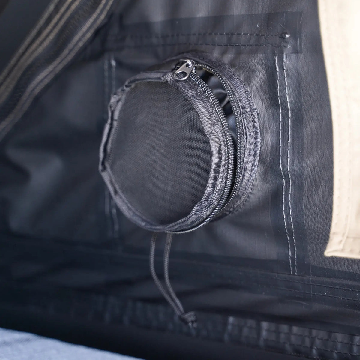 Close-up of a round, zippered mesh vent on the black wall of the CVT Mt. Hood 2 Hardshell Tent, with a beige section of the tent visible on the right—an ideal feature for outdoor adventures.