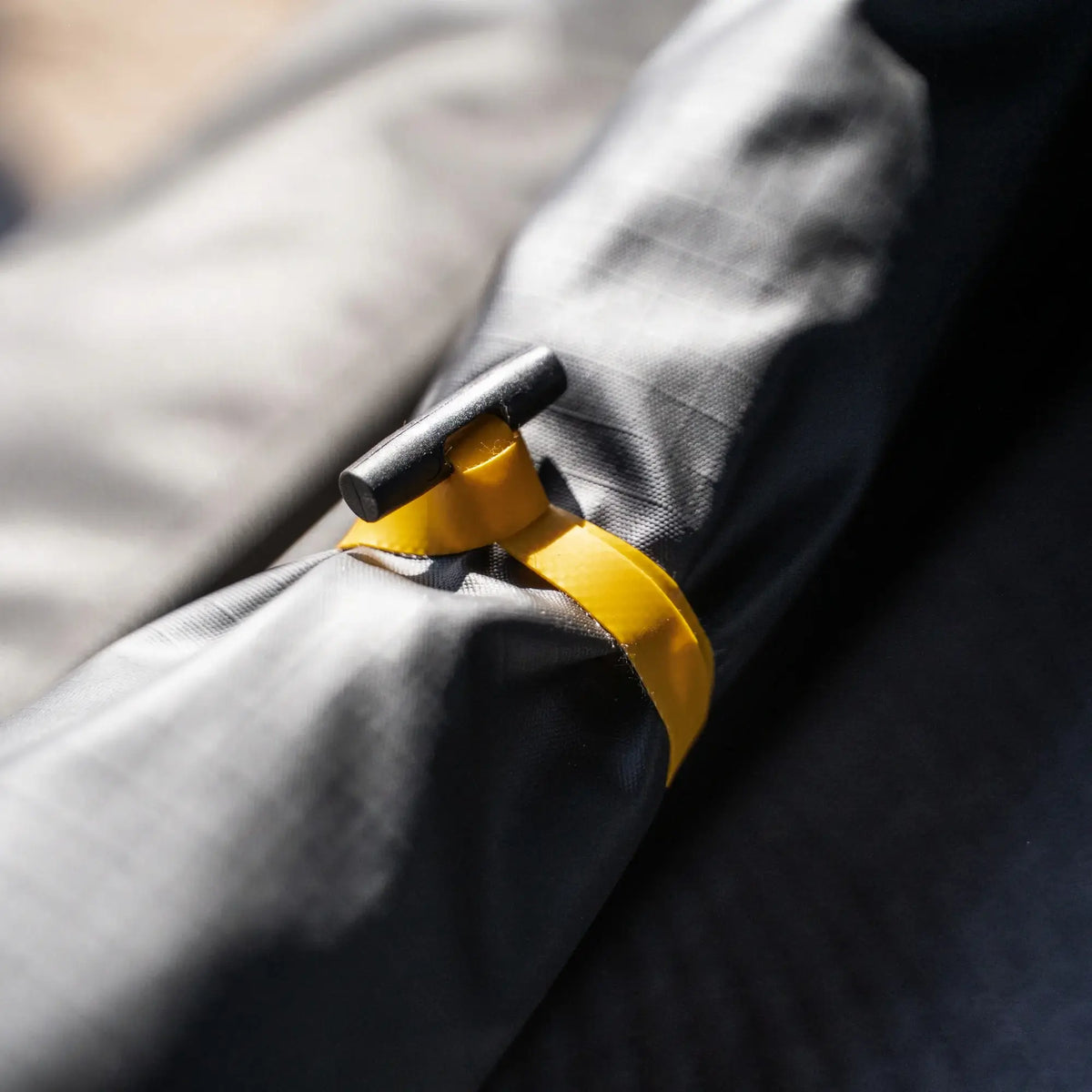 Close-up of the Mt. Hood 2 Hardshell Tent by CVT, showing a rolled-up gray fabric secured with a yellow strap and black toggle. The strap keeps the material tightly in place, demonstrating the tent’s compact and durable design—perfect for outdoor adventures and rooftop camping.