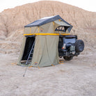 A CVT Pioneer Annex is set up atop a black SUV parked in a desert landscape with rocky hills in the background, offering an enclosed tent space for enhanced comfort and versatility.