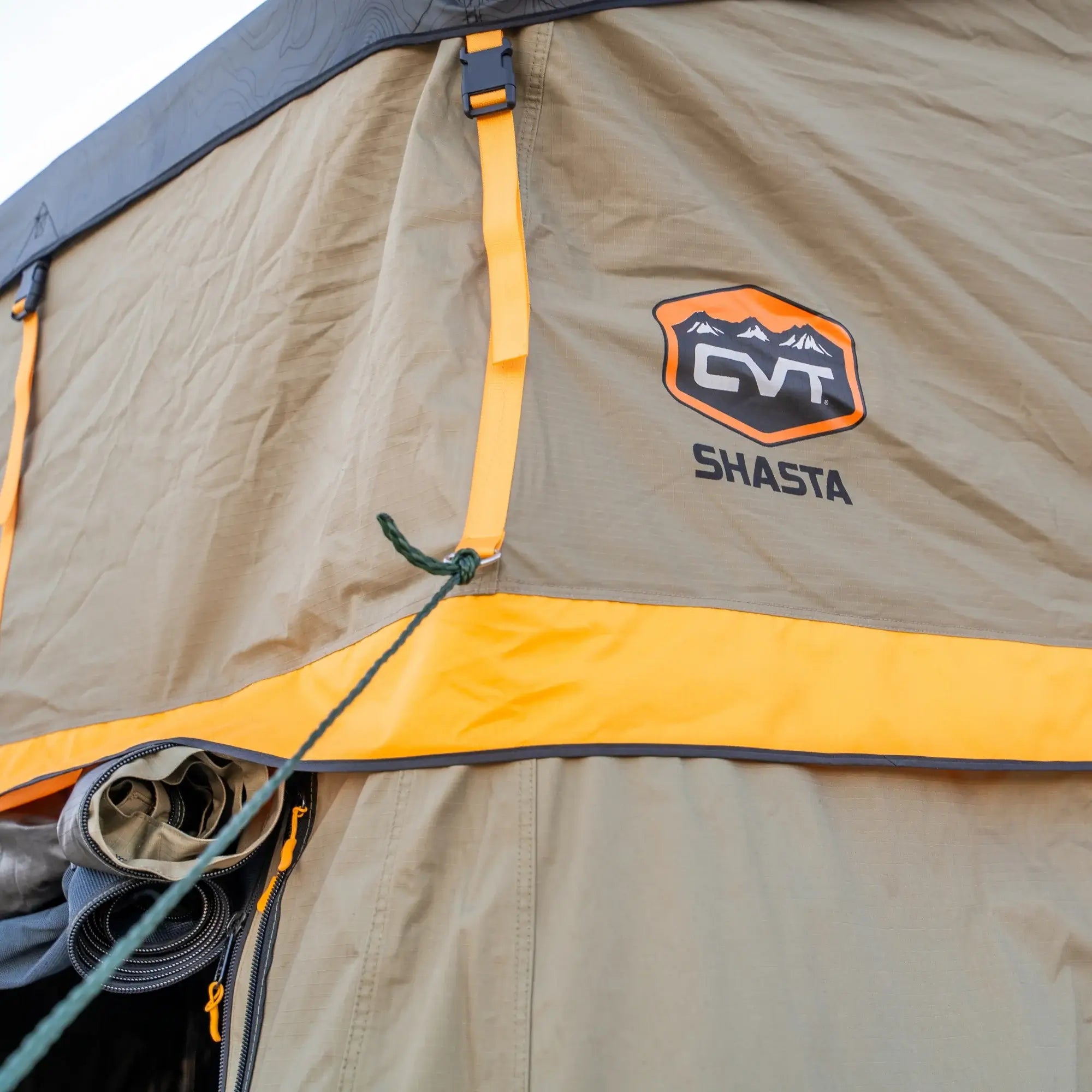 Close-up of a tan and yellow tent exterior featuring the CVT logo, orange trim, and a green rope tied to a loop. A rolled-up window cover appears on the left side. This setup is compatible with the CVT Pioneer Annex, allowing for easy expansion of enclosed tent space.