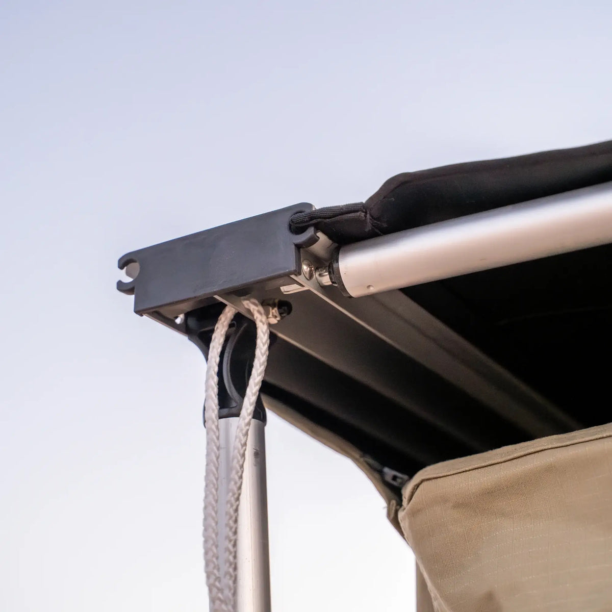 Close-up of CVT’s Pioneer Awning Walls, featuring a metal frame structure with a black fabric canopy, white rope, and beige panels crafted from waterproof ripstop material, set against a clear sky.