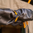 Close-up of a rolled-up black CVT Pioneer Awning Walls waterproof ripstop tarp, secured with yellow straps to a khaki-colored tent or outdoor shelter.
