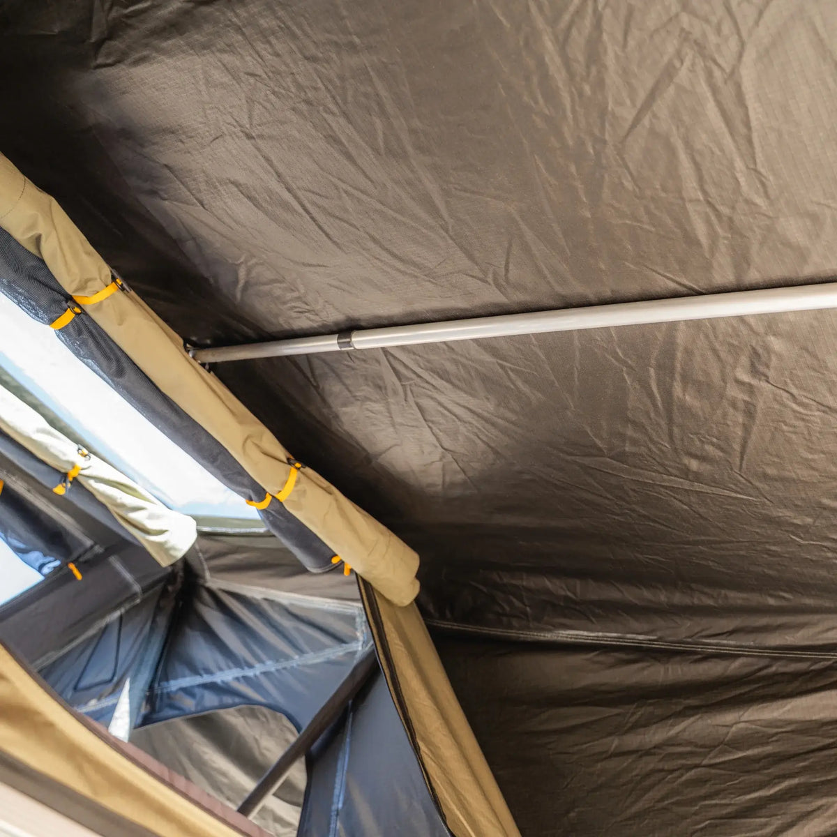 Interior view of the CVT Pioneer 2 Softshell Tent roof with sturdy metal support poles and rolled-up fabric near a window, highlighting the thoughtful construction and ample natural light—an ideal setup for overland adventures.