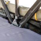 Close-up of a bed inside the CVT Pioneer 2 Softshell Tent, featuring folded support poles, a gray mattress, and olive green fabric walls with yellow straps—highlighting its ideal design for overland adventures.