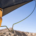 A close-up of the CVT Pioneer Spring Rod, a yellow corrosion-resistant tent pole, set up under a tent canopy with mountains and a clear blue sky in the background.