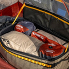 The CVT Soft Side Storage™ bag, packed with multiple Klymit sleeping bags and gear arranged neatly inside, is placed outdoors with a glimpse of a red tent in the background—providing convenient, water-resistant storage for all your adventure essentials.